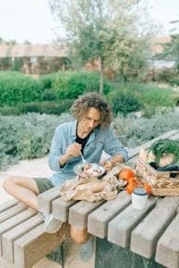 A young man sitting at a picnic table, enjoying a fresh meal surrounded by greenery.